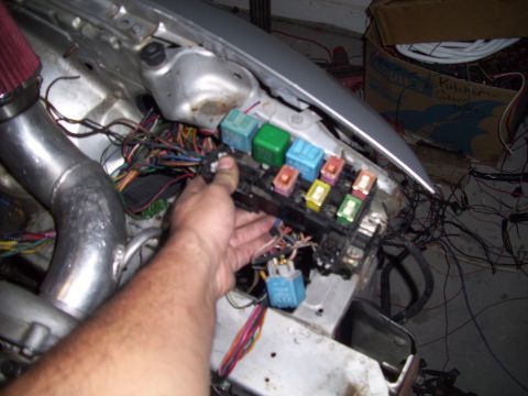 1995 Ford Probe - A hand is shown holding a fuse box filled with various colored relays and connected to a complex wiring harness.