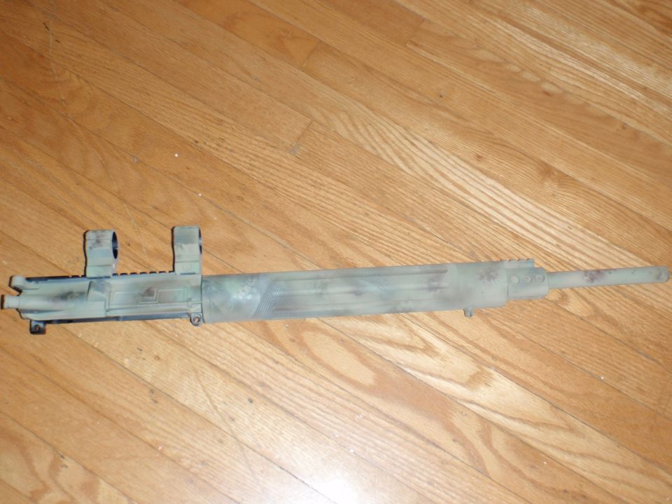 Camouflaged rifle barrel assembly with scope mounts on wooden floor