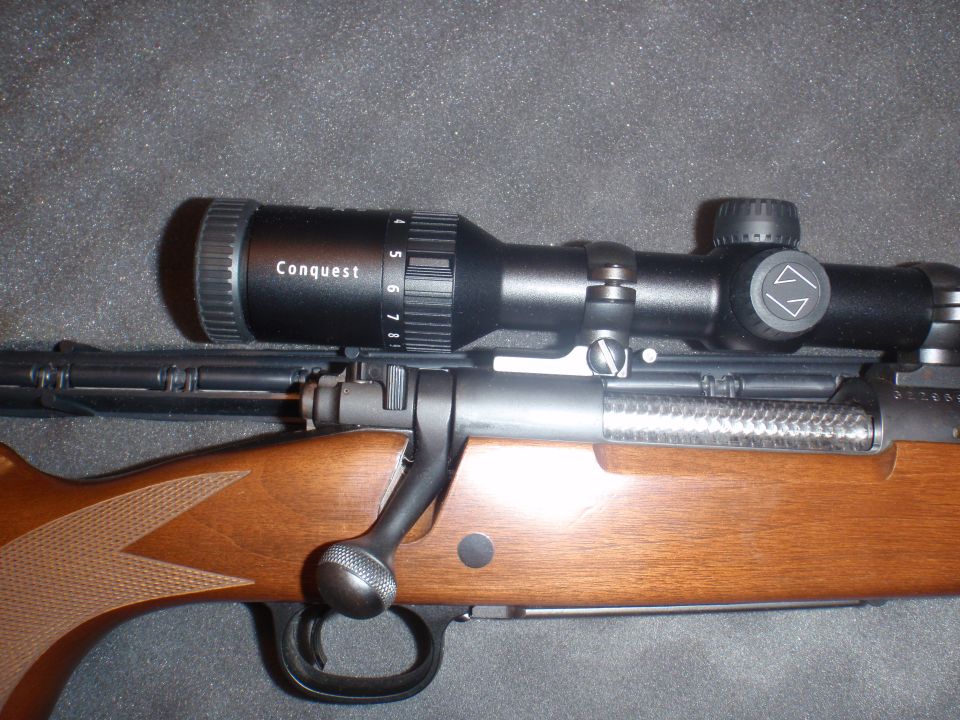 Rifle scope labeled 'Conquest' mounted on a rifle with wooden stock