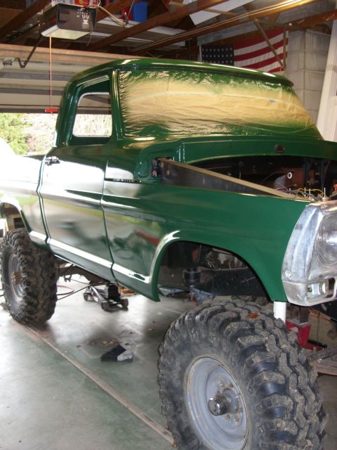 1967 Ford F-250 - A green pickup truck is undergoing work in a garage, with its hood open and windshield covered.