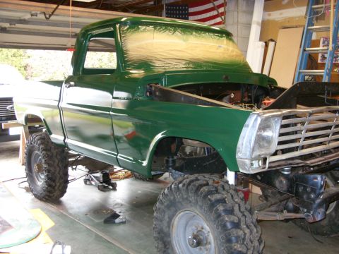1967 Ford F-250 - A green 1967 Ford F-250 pickup truck is undergoing repairs in a garage, showing its lifted suspension and off-road tires.