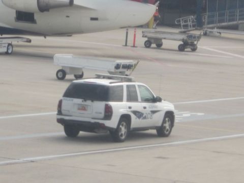 1991 Ford LTD Crown Victoria - A white police SUV is parked on an airport tarmac near a large airplane.