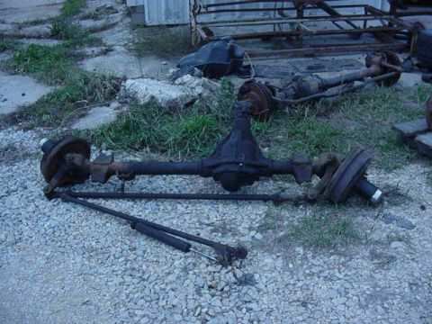 1992 Ford Bronco - Two vehicle axles with brake drums and suspension components are visible on a gravel surface.