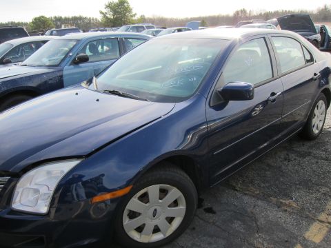 1991 Ford LTD Crown Victoria - A blue sedan with 'Stevens 150K '06' written on its windshield sits in a junkyard.