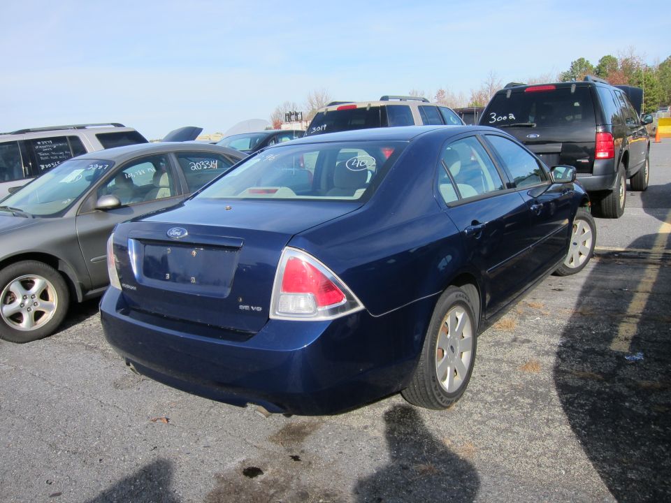 Blue Ford sedan parked in a lot, rear view. Other vehicles and a black SUV are visible
