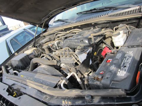 1991 Ford LTD Crown Victoria - The engine compartment of a vehicle is shown, with various mechanical parts and a battery in focus.