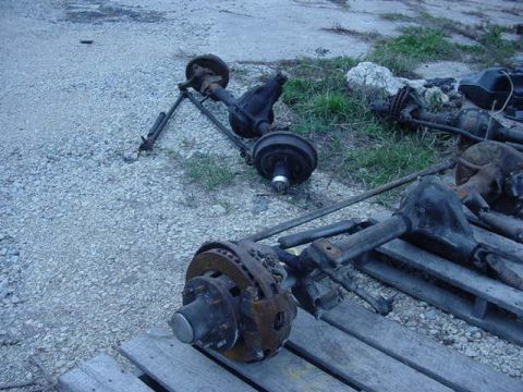 1992 Ford Bronco - Several vehicle axles and parts are laid out on gravel and wooden pallets.