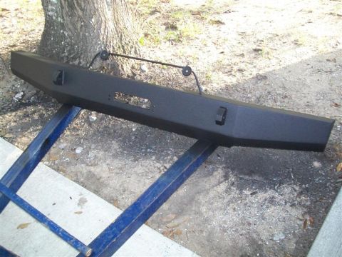 1982 Ford F-100 - Aftermarket truck bumper with winch cutout and D-ring mounts, displayed outdoors on blue stands.