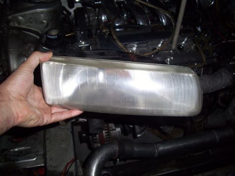 1995 Ford Probe - A person holds a clear headlight assembly, with the engine and various hoses visible in the background.