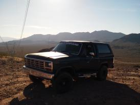 1985 Ford Bronco - This 1985 Ford Bronco is captured in a three-quarter front view against a backdrop of mountains and a clear sky.