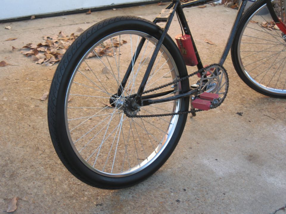 Close-up of bicycle rear wheel, chain, pedals, and red canister