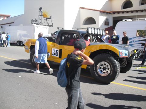 1986 Ford Bronco - A yellow off-road truck with large tires and a light bar is parked on a street, with people around.