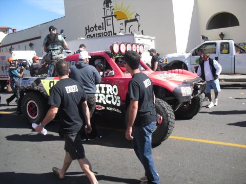 1986 Ford Bronco - A red off-road truck with "Nitro Circus" branding is seen in a crowd, with a white pickup truck in the background.