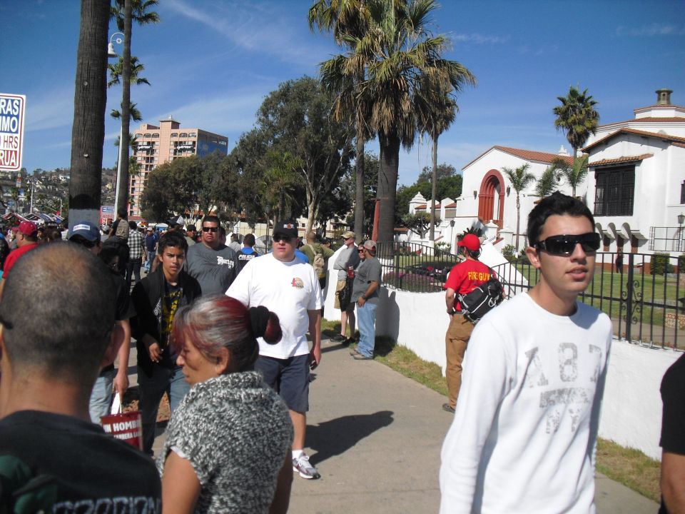 People walking on a sunny sidewalk with palm trees and buildings