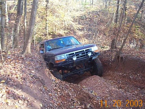1986 Ford Bronco - Ford Bronco tackles a challenging off-road trail surrounded by autumn foliage.