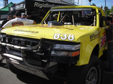 1986 Ford Bronco - A yellow off-road truck with racing decals and a light bar is parked outdoors with people around.