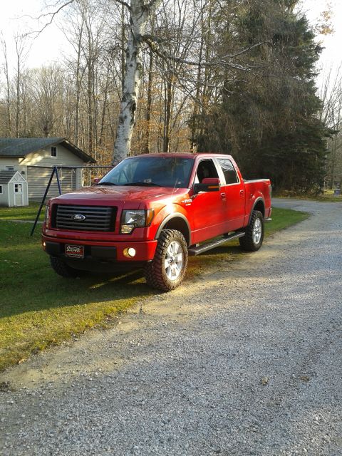 1978 Ford F-150 - This red pickup truck, likely a Ford F-150 from the late 2000s, is shown from a three-quarter front view on a gravel road.