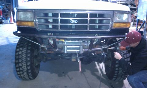 1989 Ford Bronco - A person works on the front of a 1989 Ford Bronco, which is equipped with a winch and aftermarket bumper.