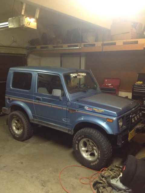 1990 Chevrolet Suburban - This Suzuki Samurai is parked inside a garage with shelves above.
