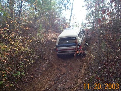 1986 Ford Bronco - White SUV navigates a steep, muddy off-road trail surrounded by autumn foliage.