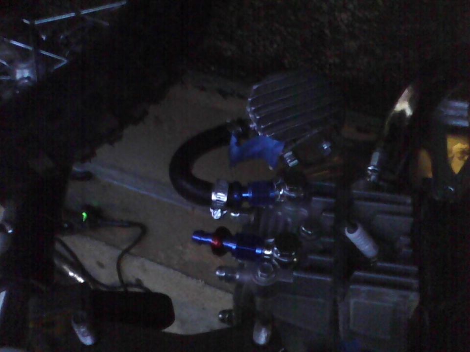 Close-up of engine components including hoses, clamps, and what looks like a spark plug. Blue fittings are visible