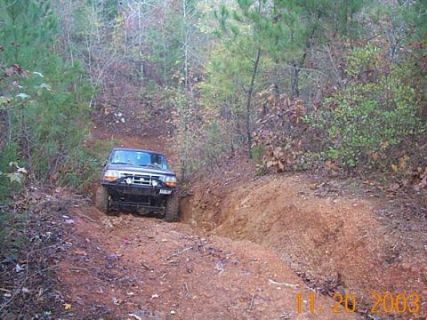 1986 Ford Bronco - A dark SUV navigates a challenging off-road trail, its grille indicating a 1992 model year.