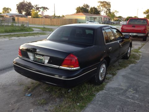 2001 Ford Crown Victoria - A black 2001 Ford Crown Victoria is parked on the side of the road, with a red pickup truck visible in the background.