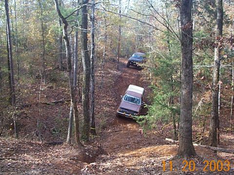 1986 Ford Bronco - Two SUVs navigate a wooded trail during an off-road excursion.