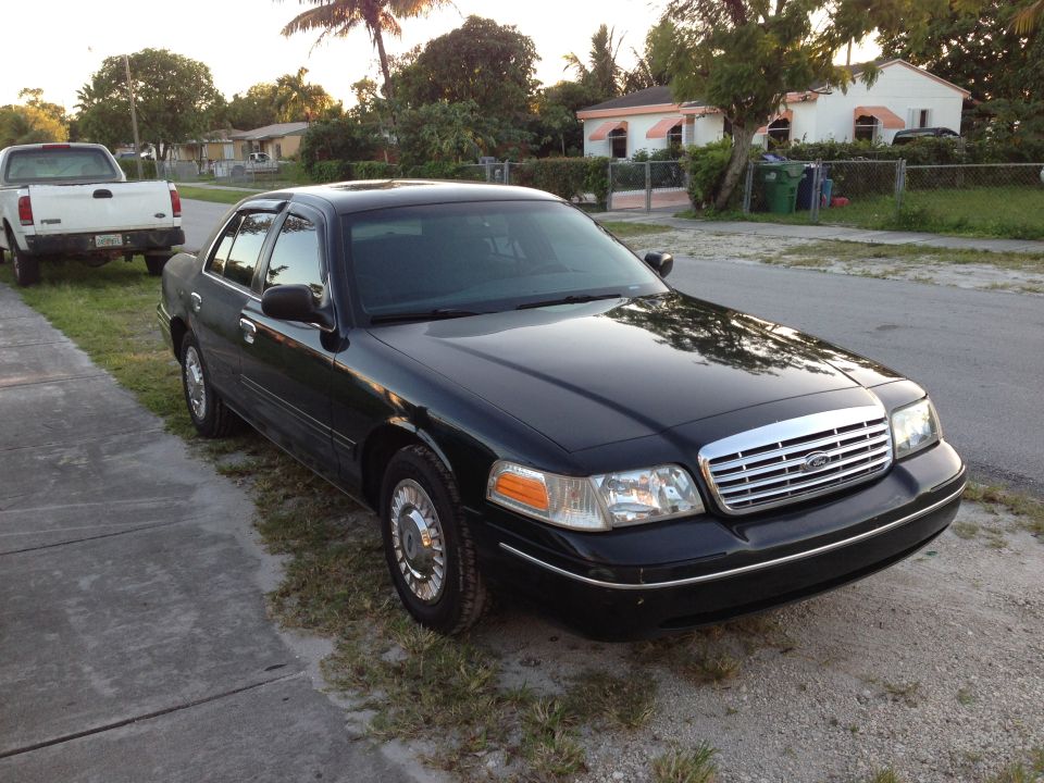 Black 2001 Ford Crown Victoria parked on a residential street, front quarter view. A white pickup truck is parked behind it