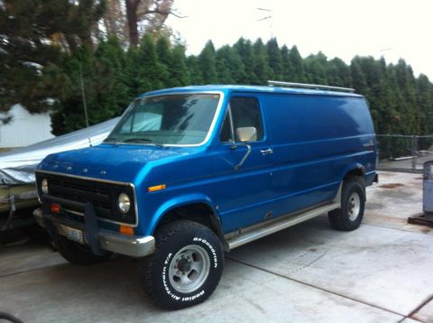 1977 Ford E350 - This blue panel van, likely from the mid-1970s, is equipped for off-road use with large tires and a roof rack.