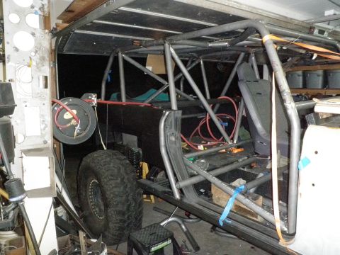1961 International Scout 800 - Custom roll cage construction inside a vehicle, with a large off-road tire and various tools visible.