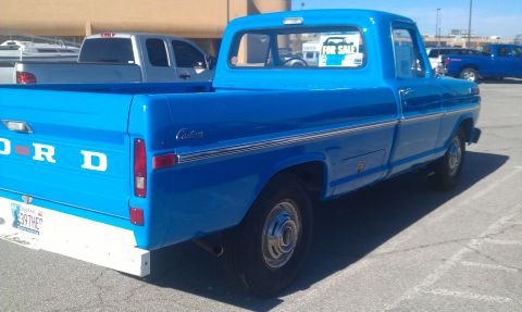 1973 Ford F-100 - A blue Ford pickup truck is parked in a lot with other vehicles, including a silver truck and a blue SUV.