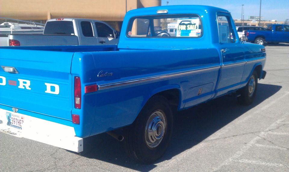 Blue Ford pickup truck, rear quarter view, white bumper, "Custom" badging