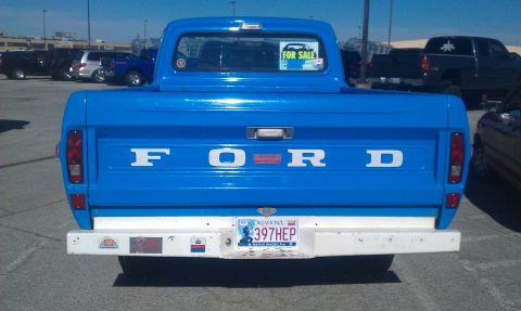 1973 Ford F-100 - This blue 1973 Ford F-100 pickup truck is seen from the rear, its iconic tailgate lettering and a 'For Sale' sign in the back window.