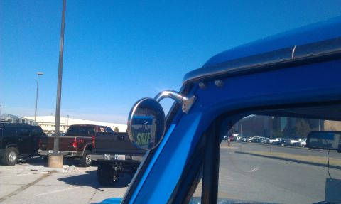 1973 Ford F-100 - A blue pickup truck's side mirror reflects a 'SALE' sign, with other vehicles visible in the background.