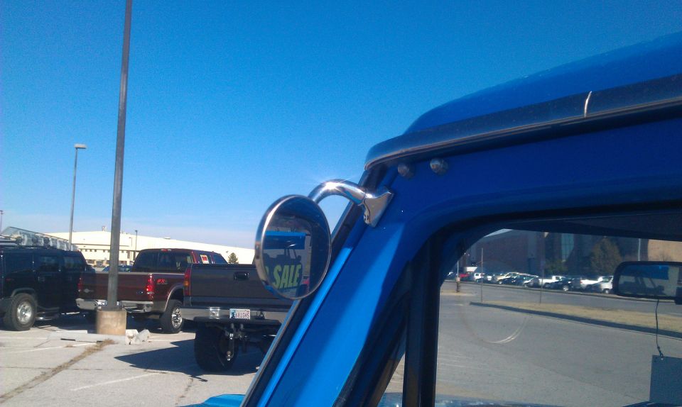 Side mirror on blue pickup truck shows a 'SALE' sign. Other trucks and SUVs are parked in lot