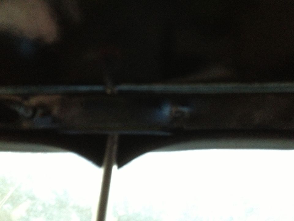 Underside of a dark-colored vehicle frame with visible bolts and a metal rod. A thin pole extends upwards from below