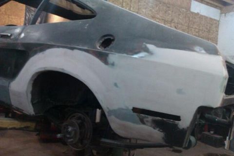 1978 Ford Mustang II - The rear section of a car is undergoing bodywork, with primer and filler applied to the quarter panel.