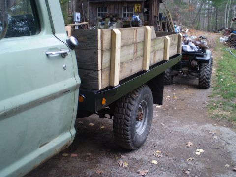 1979 Ford Bronco - A flatbed truck with a custom wooden bed is parked next to a workshop, with an ATV hitched behind it.