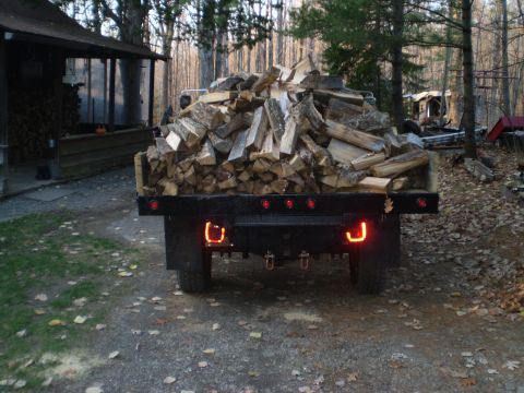 1979 Ford Bronco - Flatbed truck carrying a large load of firewood, parked in a wooded area.