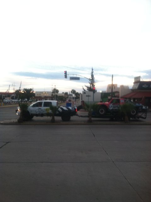 2004 Ford F-150 - A white pickup truck tows a race truck on a trailer down a street.