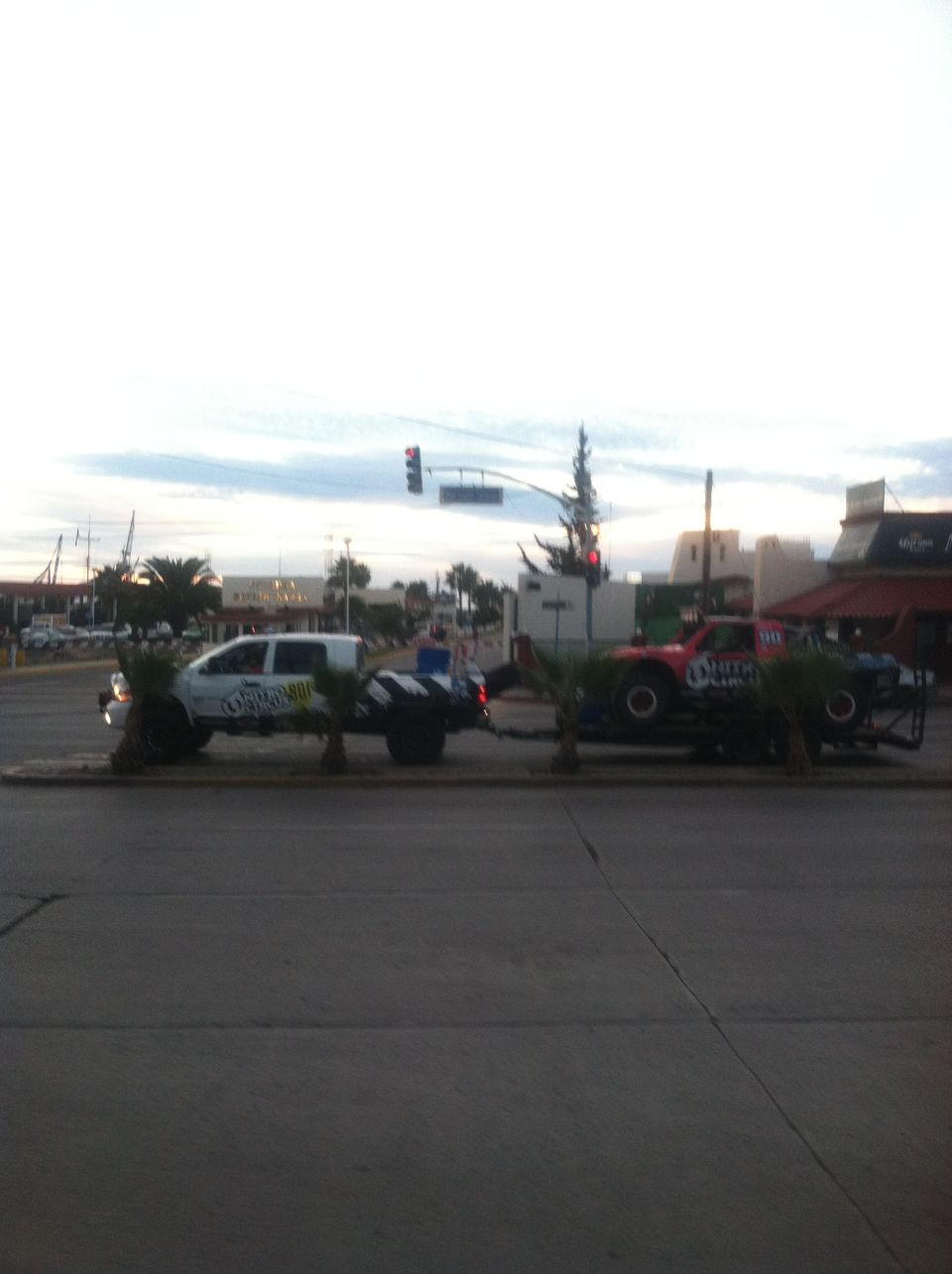 White pickup truck towing a red and blue race truck on a trailer