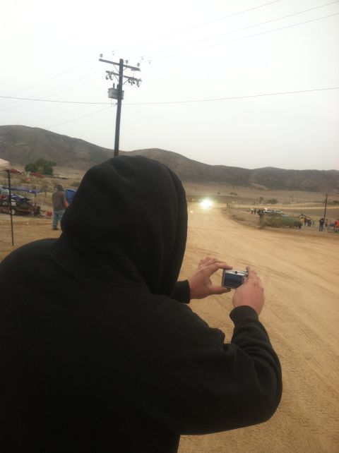 2004 Ford F-150 - A person films a dusty off-road race event with multiple vehicles and spectators in the distance.