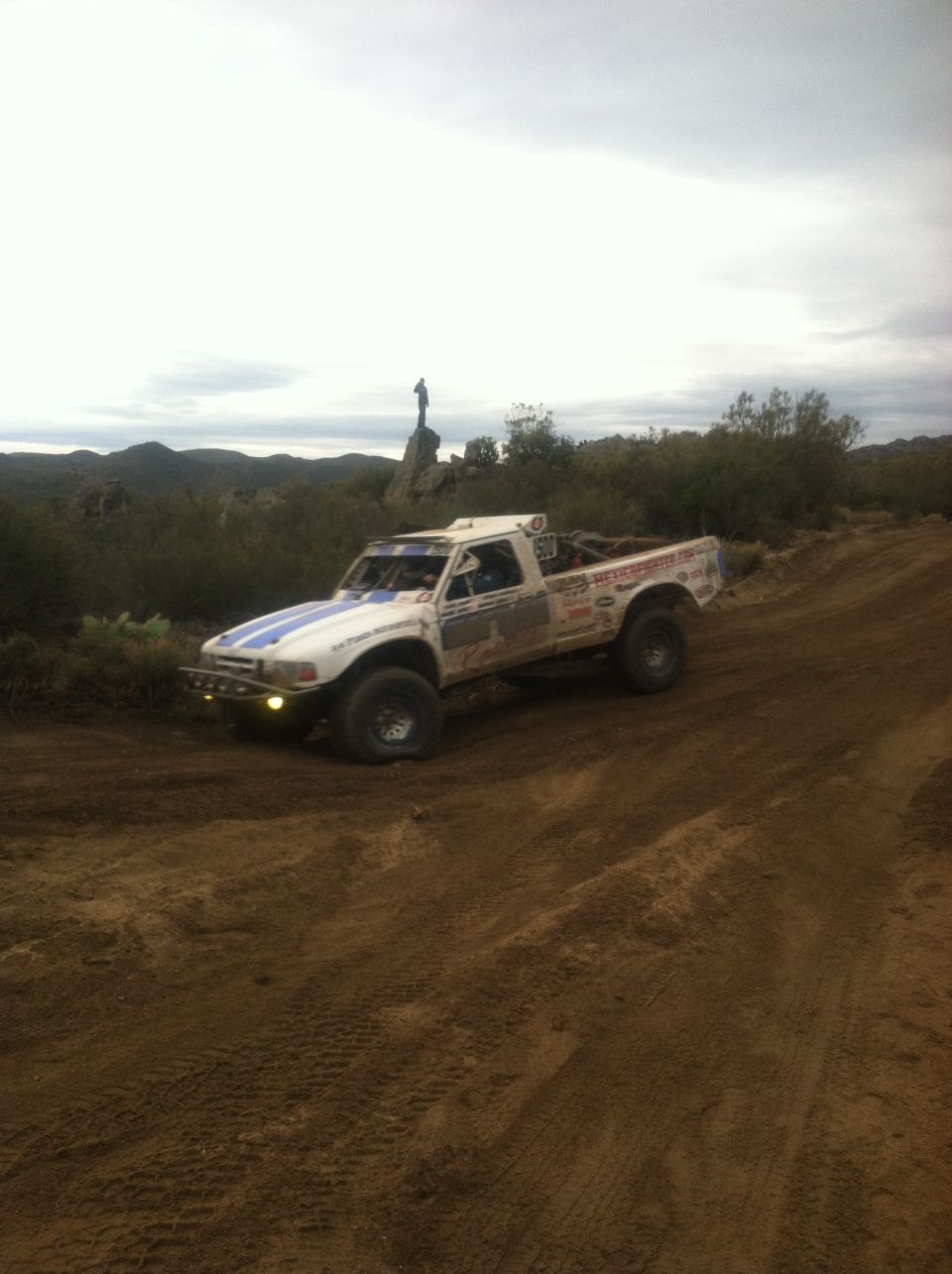 White off-road truck with blue stripes and racing decals on a dirt track