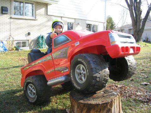 1986 Ford Bronco - A child sits in a red toy truck, giving a thumbs up while perched on a tree stump.