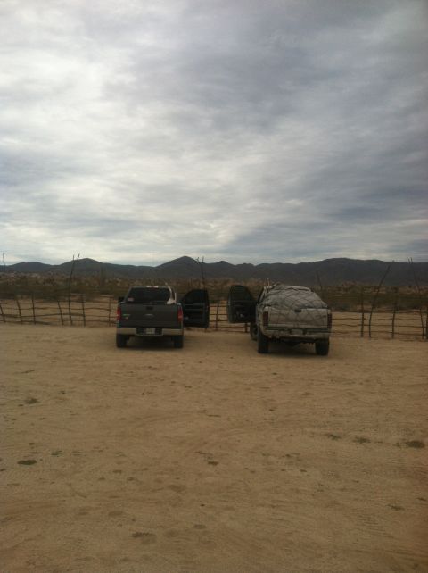 2004 Ford F-150 - Two trucks are parked in a dusty lot with mountains in the background under a cloudy sky.