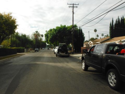 1979 Ford Bronco - A dark gray Ford F-150 pickup truck tows a white Jeep Wrangler on a trailer down a suburban street.