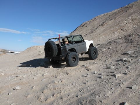 1979 Ford Bronco - An off-road SUV navigates a rocky, desert terrain under a clear blue sky.