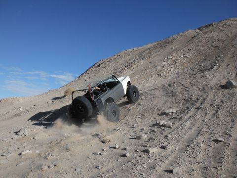 1979 Ford Bronco - An off-road vehicle navigates a steep, rocky incline under a clear blue sky.