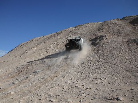 1979 Ford Bronco - A vehicle ascends a rocky, barren slope under a clear blue sky.
